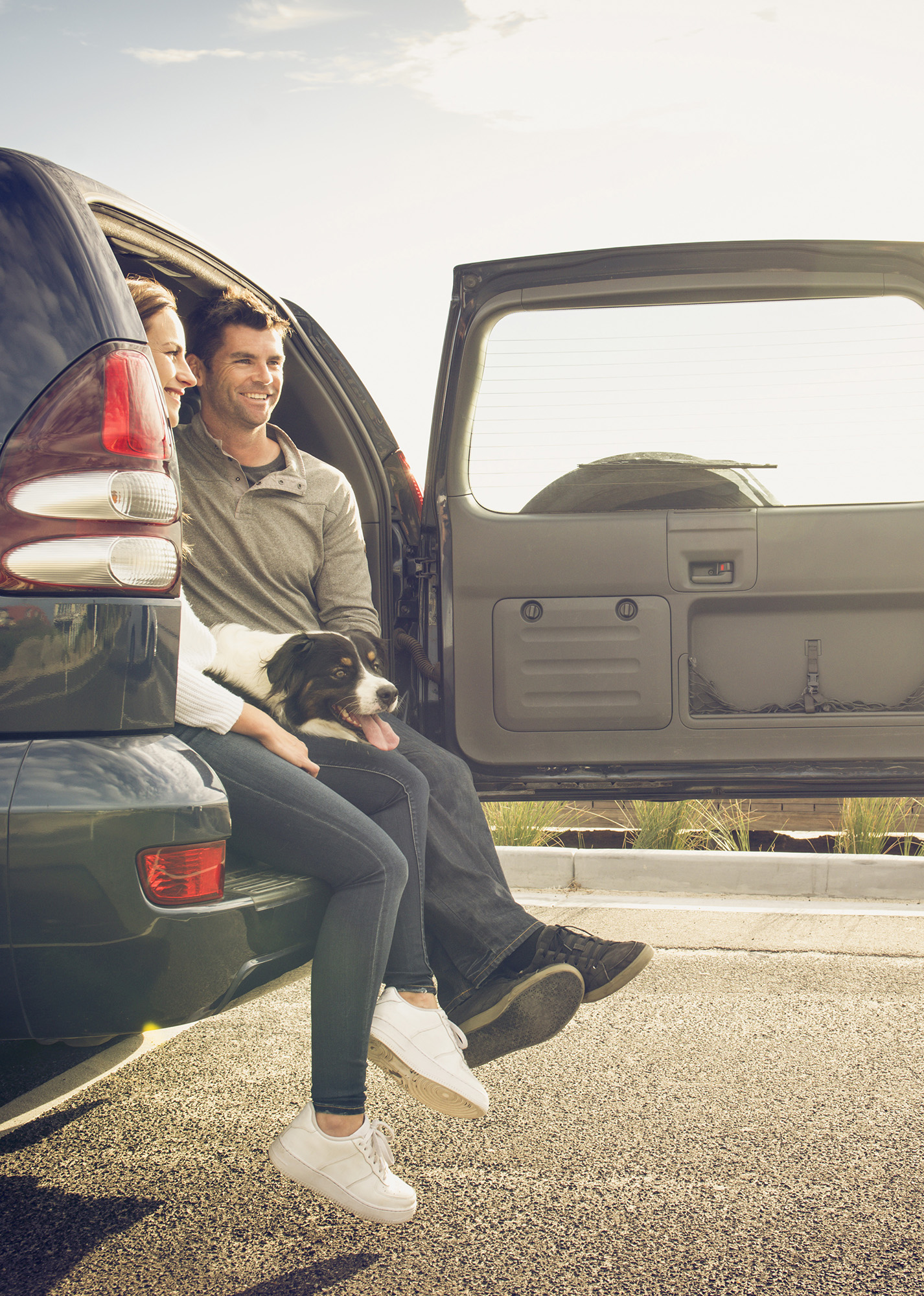 Man and woman with their dog sitting in back of vehicle.