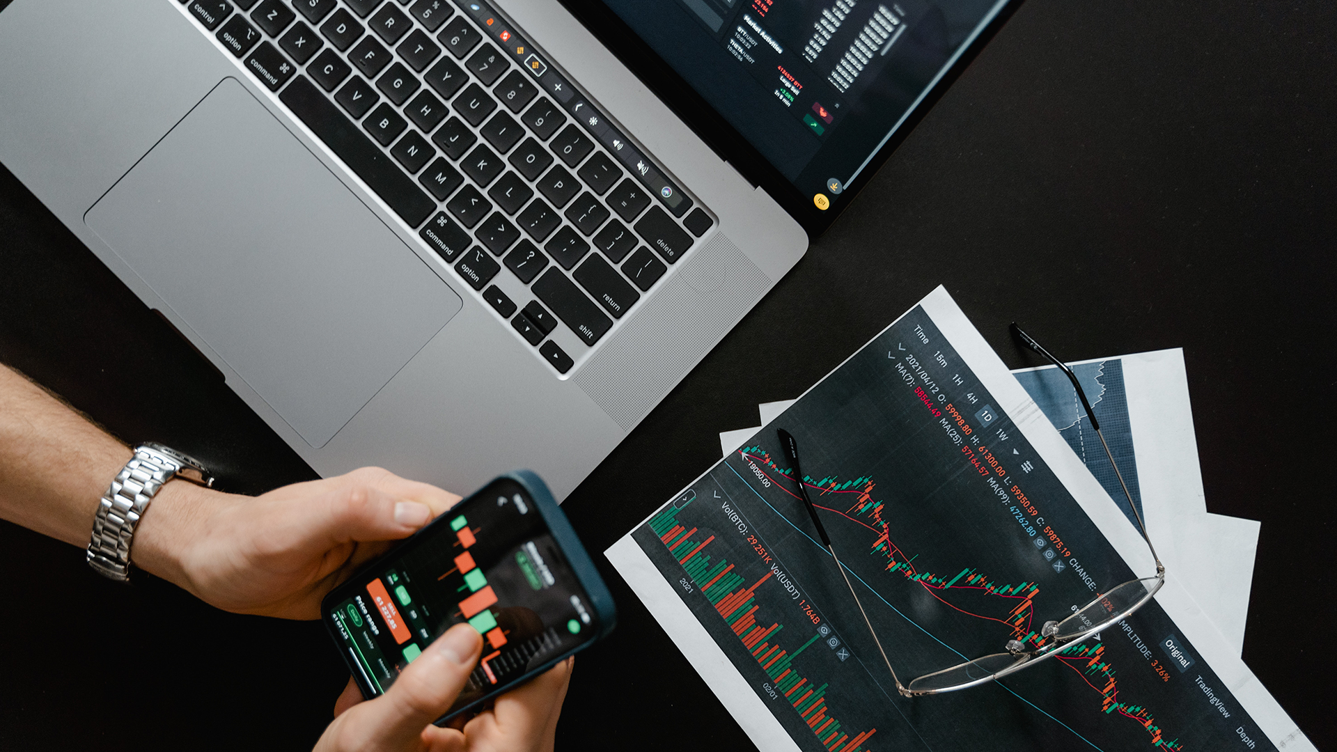 Person holding a phone with stock market printouts on table