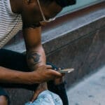 man sitting on stoop scrolling through his phone holding a denim jacket