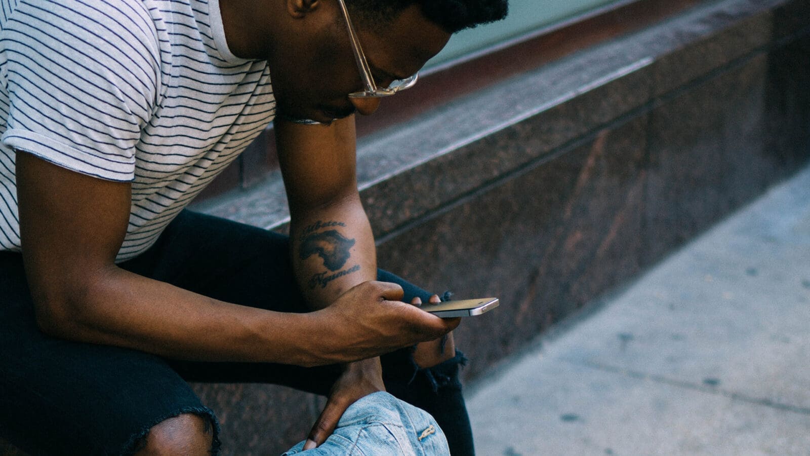 man sitting on stoop scrolling through his phone holding a denim jacket