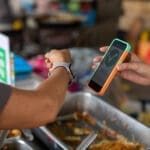 person using watch to pay for food at a market with a phone reading out a checkmark.