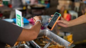 person using watch to pay for food at a market with a phone reading out a checkmark.