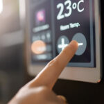 A finger tapping a screen to lower the temperature by using an ipad mounted to the wall for the thermostat.