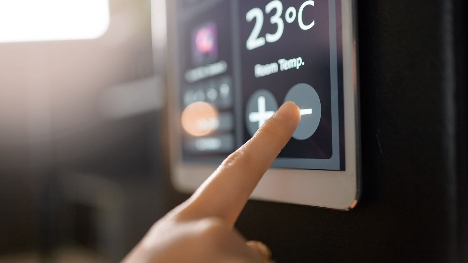 A finger tapping a screen to lower the temperature by using an ipad mounted to the wall for the thermostat.