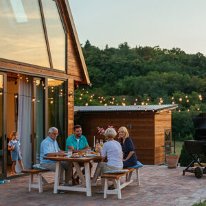 A family sitting on patio behind house next to BBQ grill.